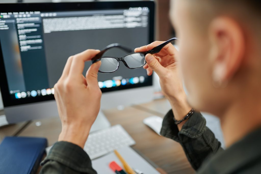 Male IT specialist holds glasses at pc monitor